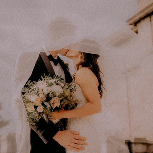 Dreamy photograph of bride and groom kissing during wedding day under veil