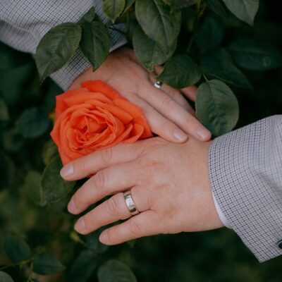 LGBTQ+ wedding photography of two men holding hands around a rose wearing wedding rings