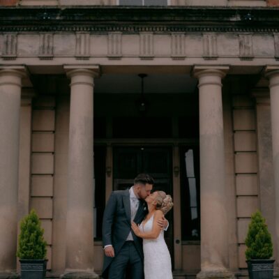 Wide shot of Pendrall Hall with Bride and Groom kissing outdoors in embrace
